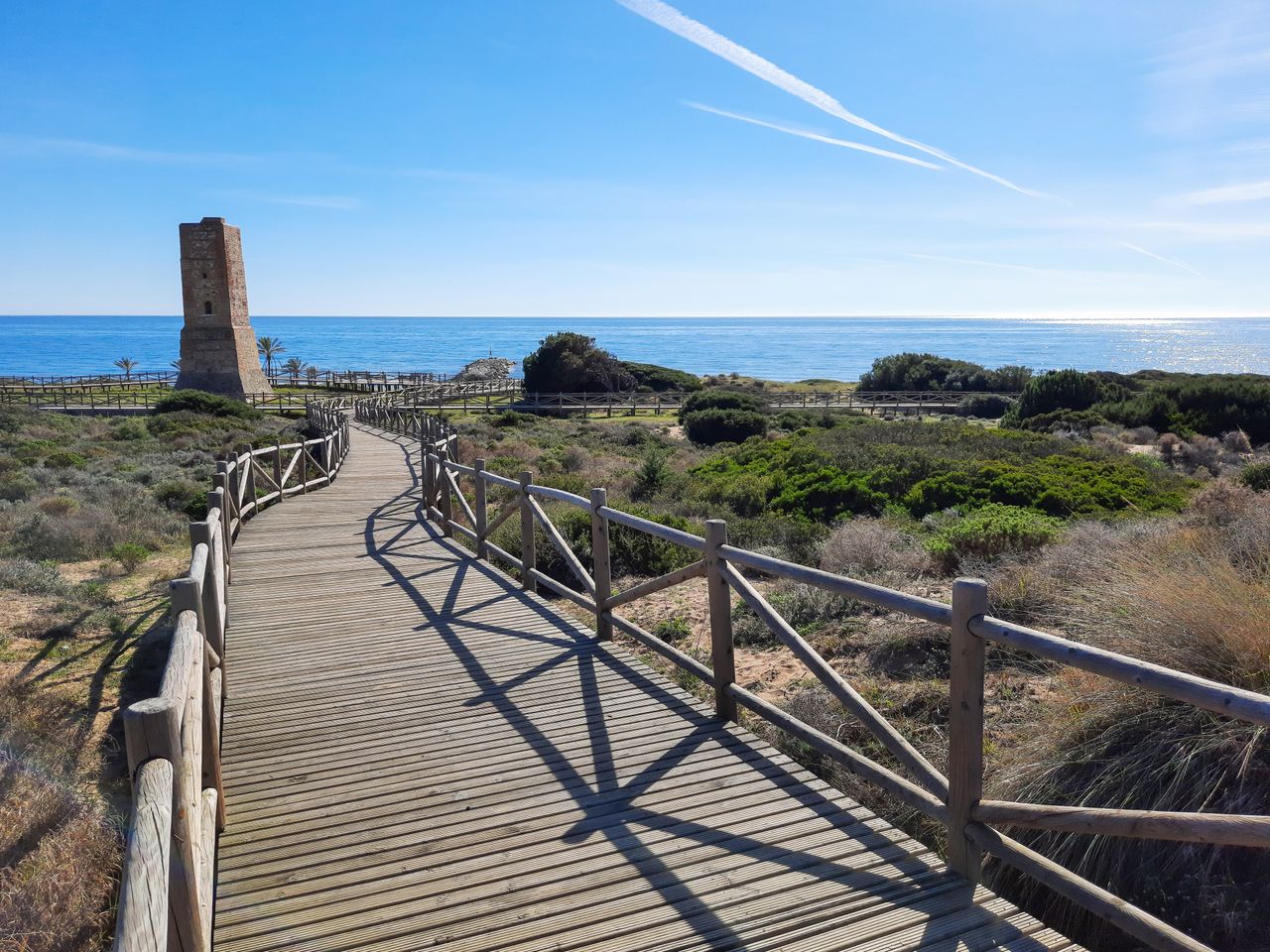 Playa de Cabopino in Marbella, Málaga, featuring golden sand, clear Mediterranean waters, pine trees, and the protected Artola sand dunes.